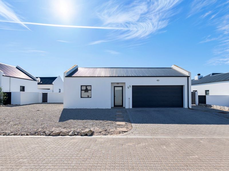 Modern single-story house exterior featuring a clean white facade, dark metal roof, paved driveway, and a secure roller garage door.
