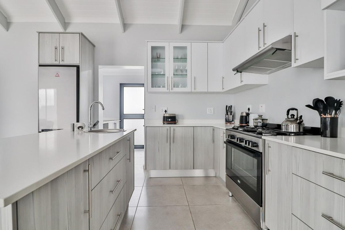 Modern kitchen featuring light wood-grain cabinetry, stone countertops, a central island, and high-quality stainless steel appliances under an exposed beam ceiling.