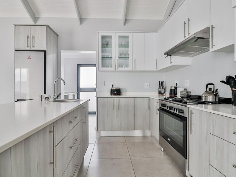Modern kitchen featuring light wood-grain cabinetry, stone countertops, a central island, and high-quality stainless steel appliances under an exposed beam ceiling.