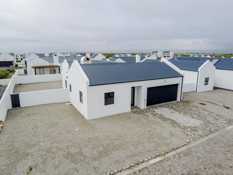 Aerial view of a modern single-story residential property featuring a corrugated metal roof, attached garage, and gravel yard within a housing estate.