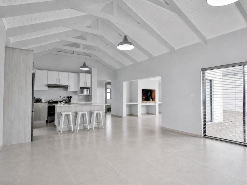 Spacious open-plan living area featuring a modern kitchen with island, vaulted ceilings with exposed rafters, and seamless access to the outdoor patio.