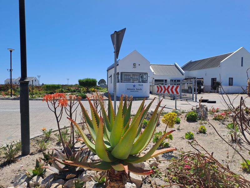 The entrance to Atlantic Sands Private Estate featuring a security guard house, paved driveway, and landscaped garden area.
