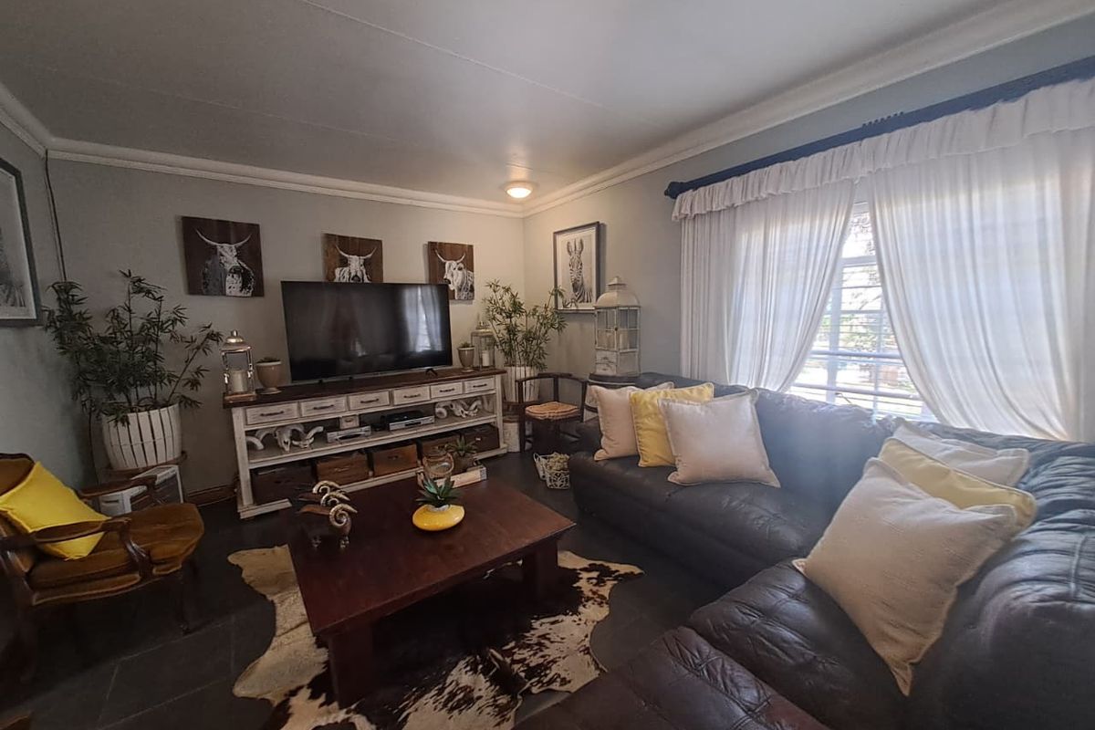 A comfortable living room featuring tiled flooring, crown molding, and large windows with curtains, providing a cozy space for relaxation.