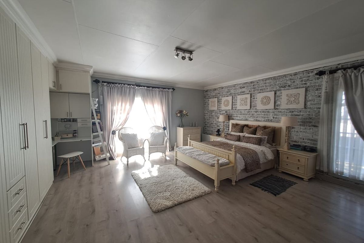 Spacious bedroom featuring built-in cabinetry, a dedicated desk area, and a decorative brick-style feature wall with neutral laminate flooring.