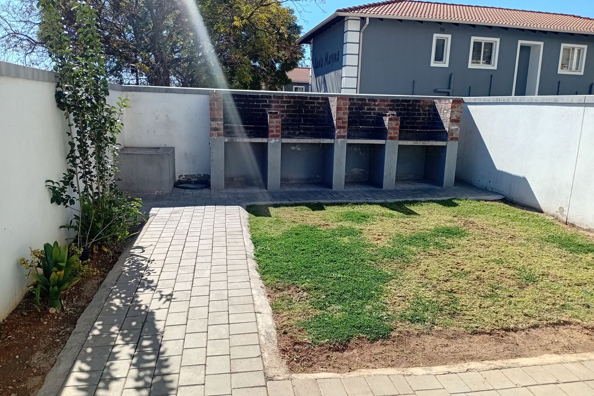A private rear courtyard featuring a built-in brick braai area, paved walkway, and a small lawn section enclosed by boundary walls.