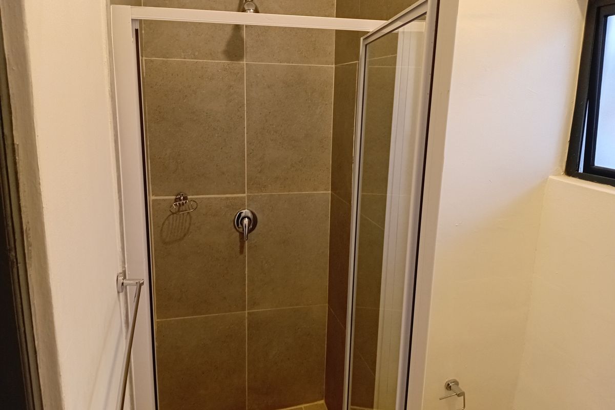 A clean, functional bathroom shower area featuring neutral-toned wall and floor tiles, a glass shower enclosure, and modern chrome fixtures.