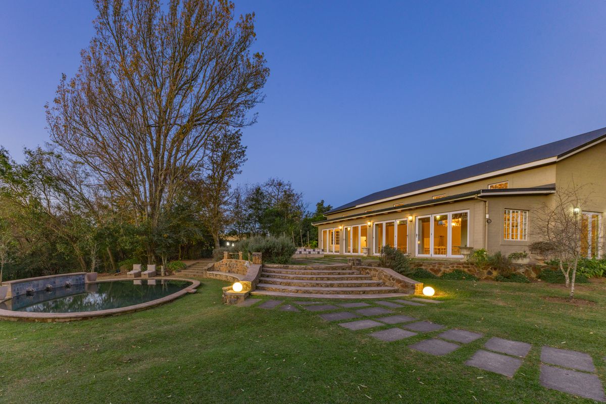 Rear view of the farmhouse featuring a landscaped garden, stone staircase, paved pathways, and a swimming pool with integrated exterior lighting.