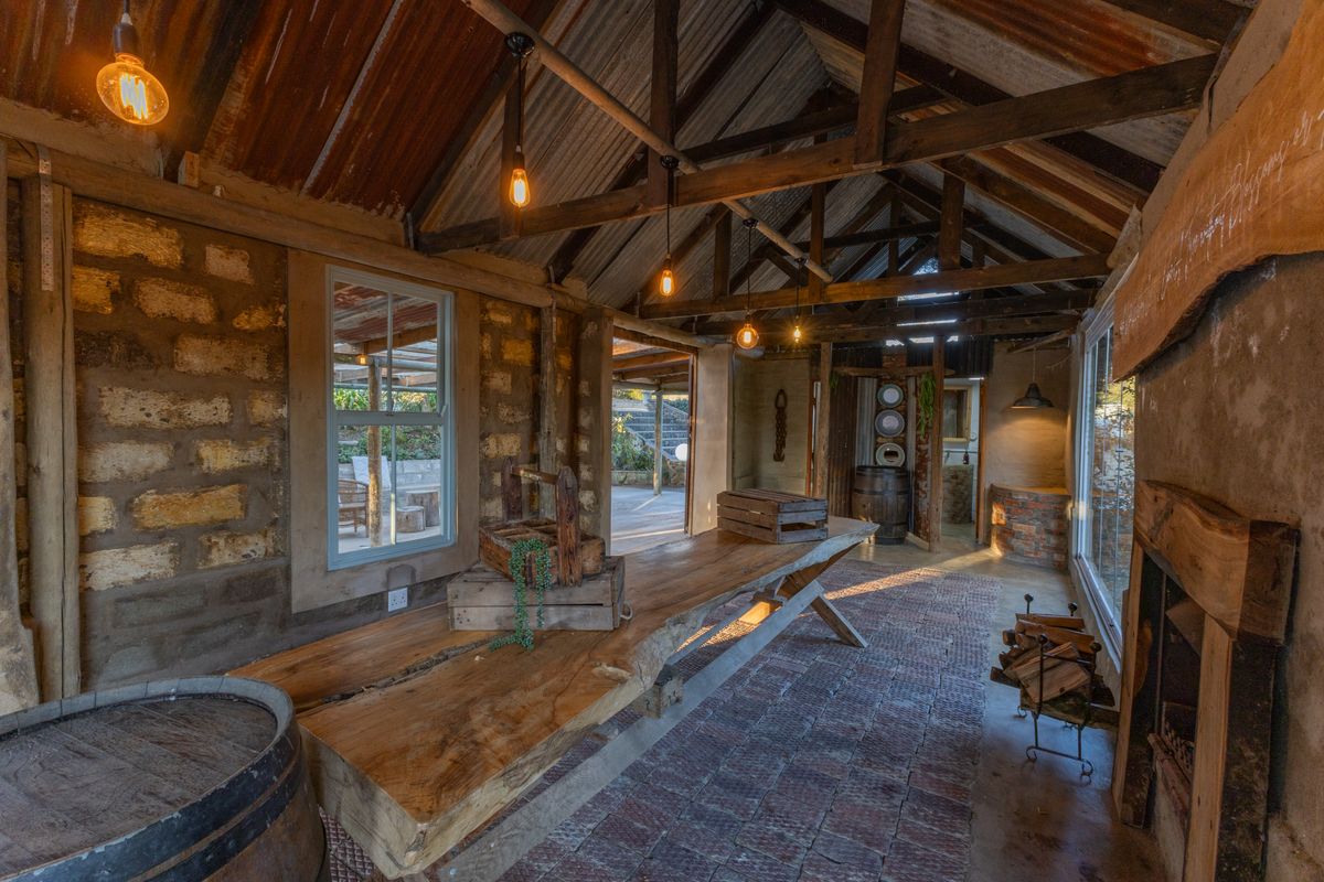 Rustic living space featuring exposed timber roof trusses, stone masonry walls, brick flooring, and a fireplace, creating a warm and authentic farm-style atmosphere.