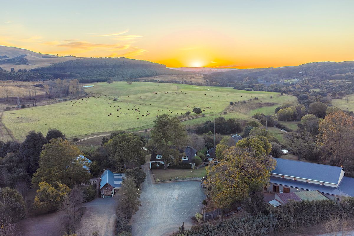 Aerial view of a sprawling farm property featuring a main residence, multiple outbuildings, gravel driveway, and extensive grazing paddocks at sunset.