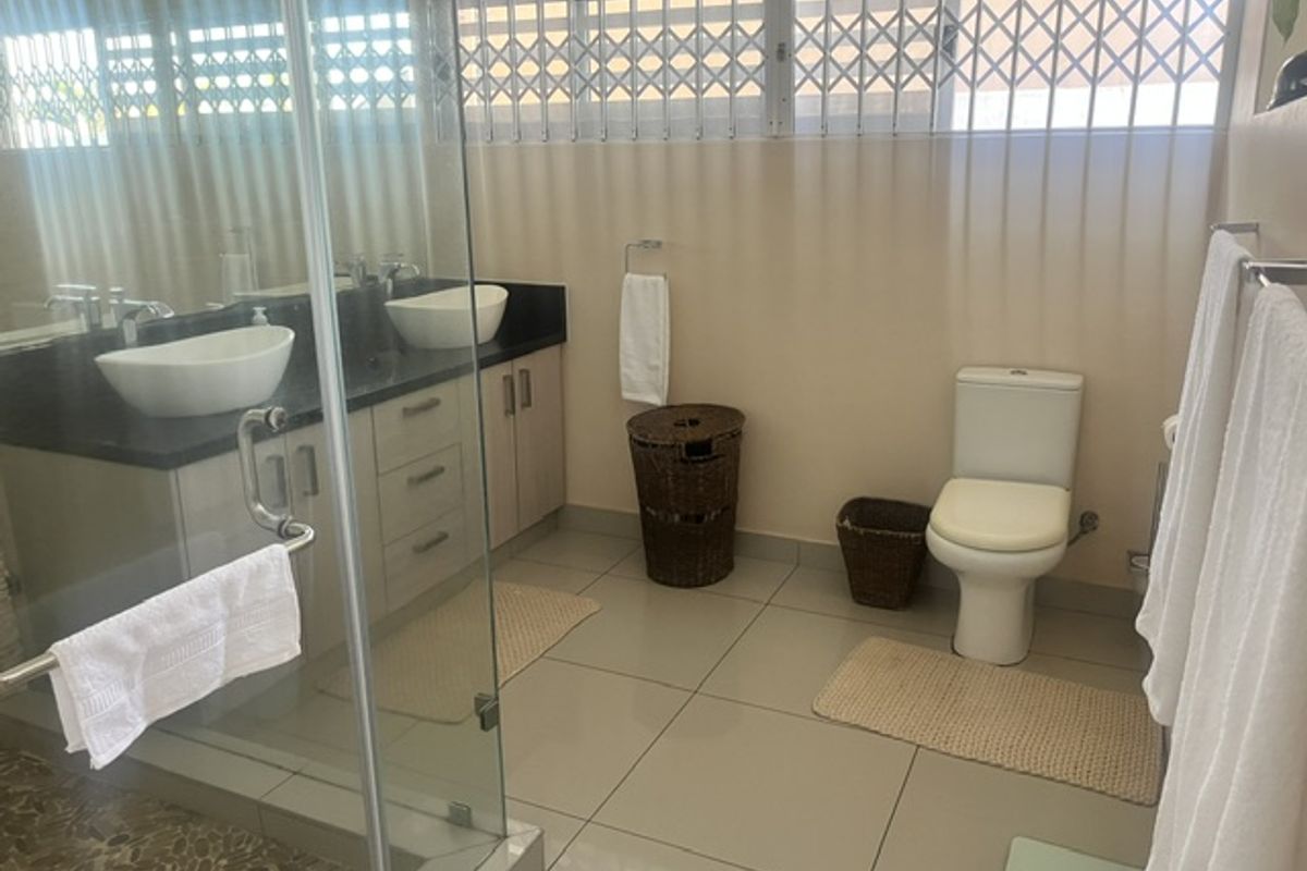 A well-maintained bathroom featuring a double vanity with vessel sinks, granite countertops, a glass-enclosed shower, and tiled flooring.