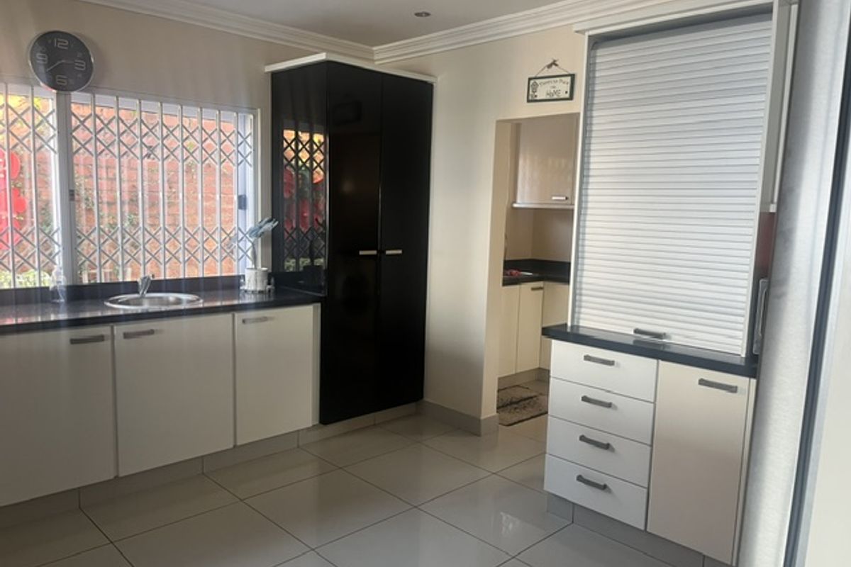 Modern kitchen featuring high-gloss cabinetry, tiled flooring, integrated appliance storage with roller shutter, and security bars on the window.