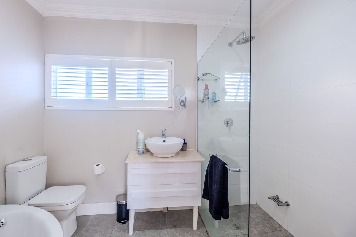 Modern bathroom featuring a vessel sink on a vanity cabinet, a glass-enclosed walk-in shower with a rain shower head, and white shutter window treatments.