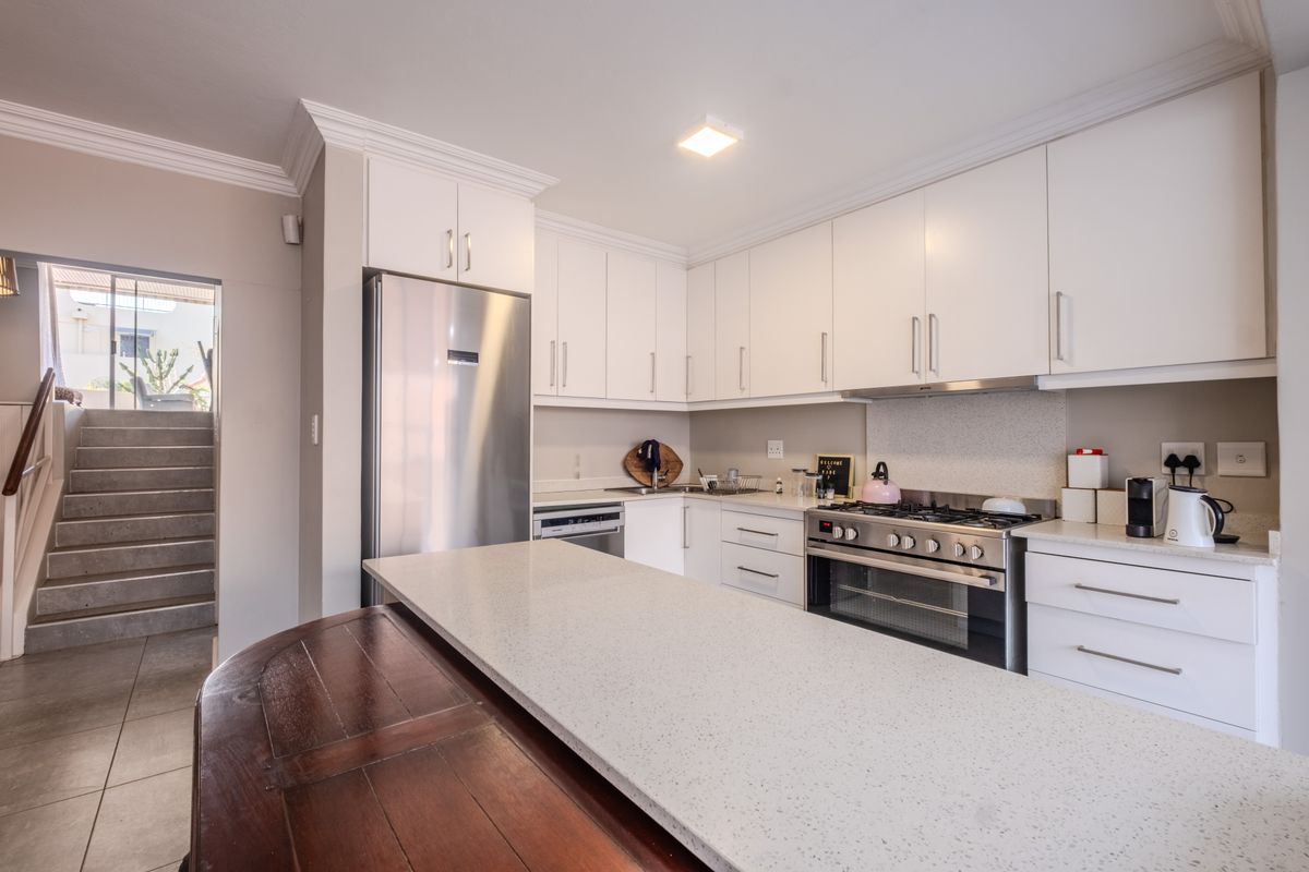 Modern kitchen featuring white cabinetry, stone countertops, stainless steel appliances, and a breakfast bar, with an adjacent staircase leading to an outdoor area.