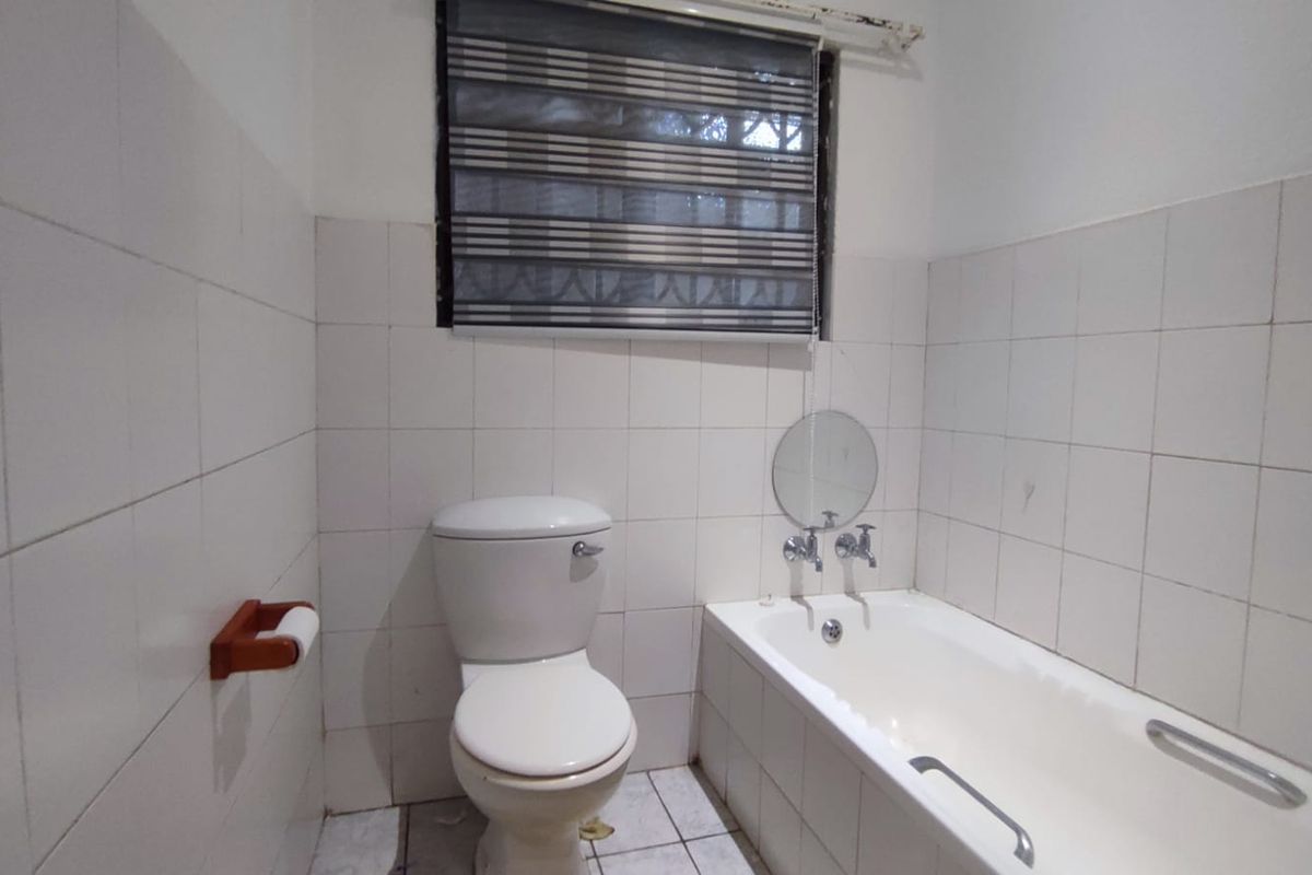 A functional bathroom featuring a standard bathtub, toilet, and full-height wall tiling, requiring cosmetic updates to improve its overall condition and aesthetic appeal.