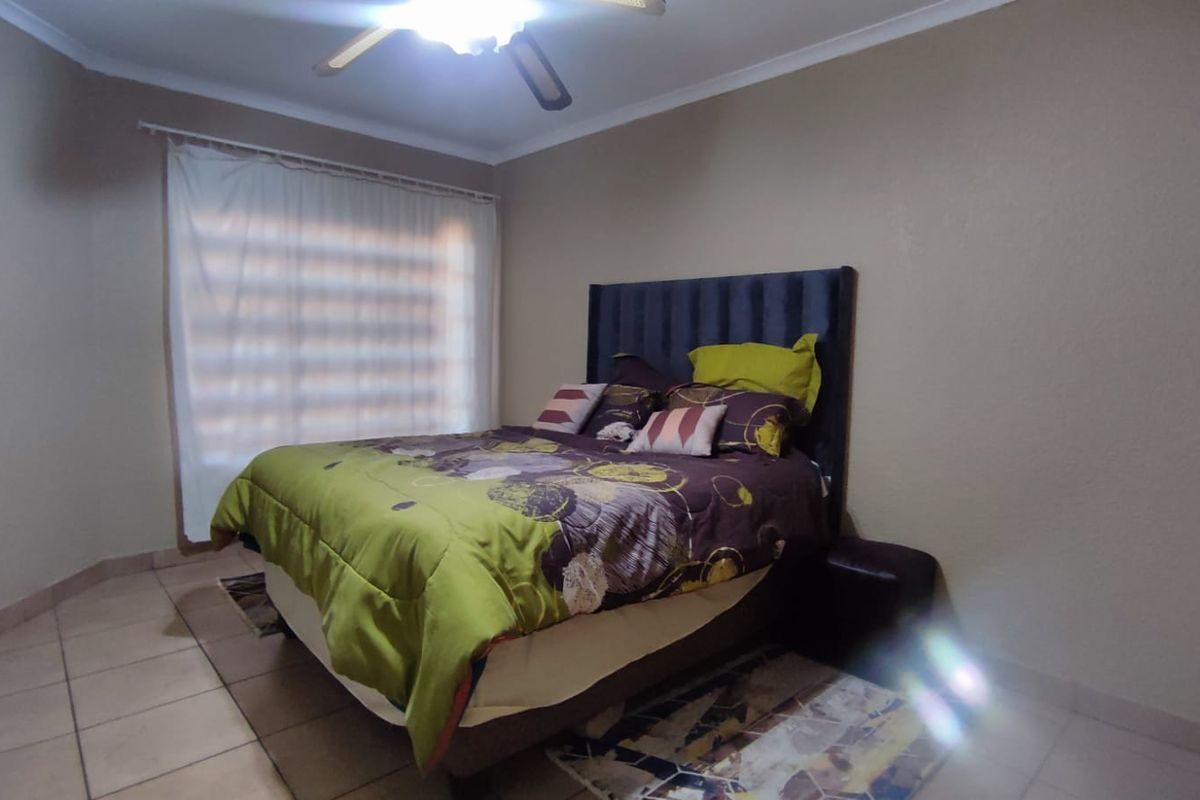 A standard bedroom featuring tiled flooring, a ceiling fan, and a large window with curtain rails, providing a functional and neutral living space.