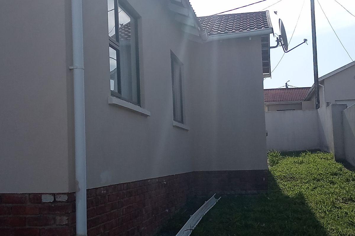 Side view of the house exterior featuring plastered walls, a brick plinth, and visible roof tile damage.