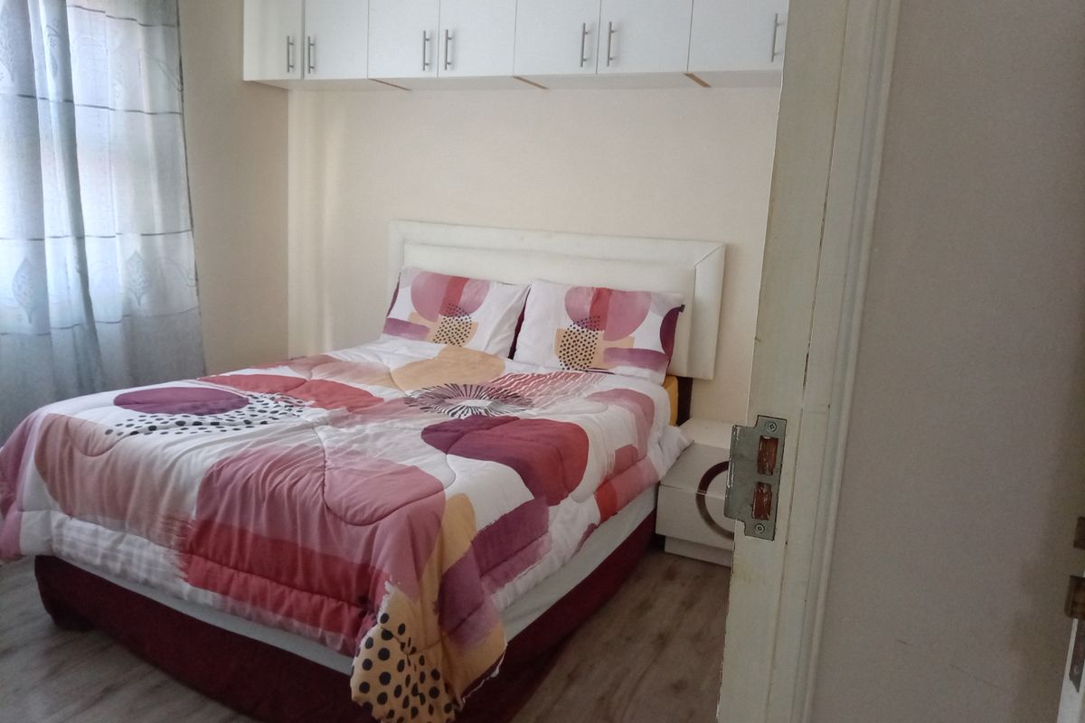A bedroom featuring light-toned laminate flooring and white built-in overhead storage cabinetry above the bed area.