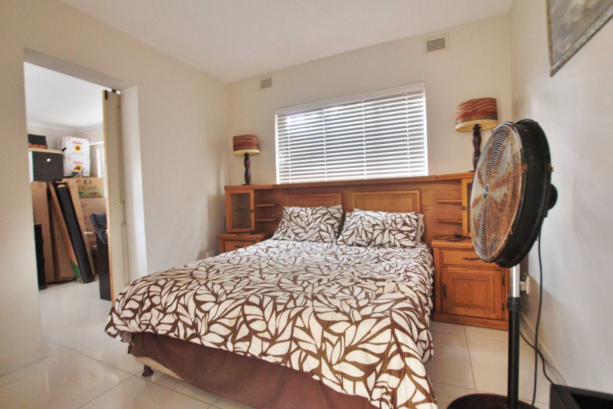 A bedroom featuring built-in timber headboard cabinetry and tiled flooring, with an adjacent room visible through the doorway.