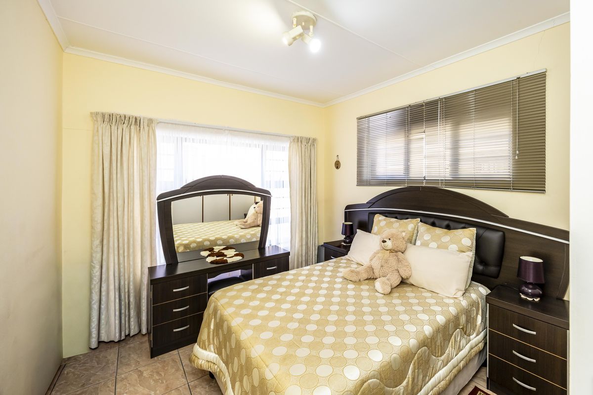 A standard bedroom featuring tiled flooring, neutral wall paint, and window treatments including venetian blinds and curtain rails.