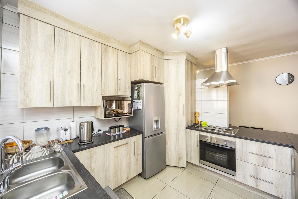 Modern kitchen featuring light wood-grain cabinetry, dark countertops, stainless steel appliances including a gas hob, oven, and extractor fan, with neutral tiled flooring.