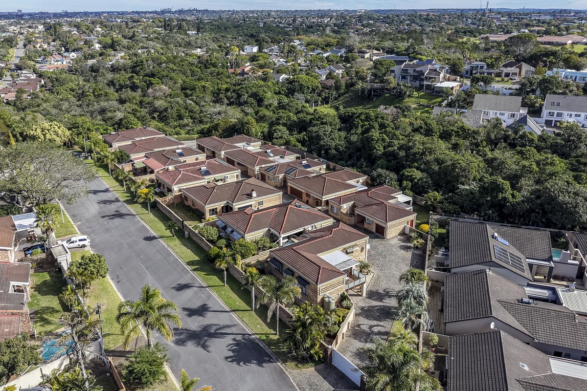 Aerial view of a residential townhouse complex featuring multiple units with tiled roofs, paved driveways, and established surrounding greenery.