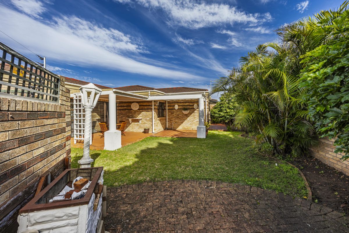 Rear garden featuring a covered patio, brick paving, lawn, and a built-in braai area, enclosed by brick boundary walls.