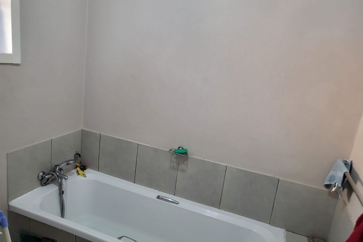 A functional bathroom featuring a standard bathtub with tiled splashback and chrome fixtures, requiring minor maintenance and cosmetic updates.