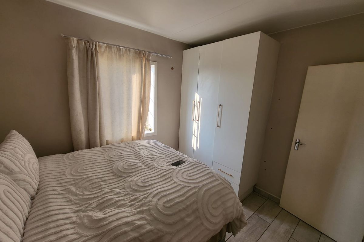 A bedroom featuring tiled flooring and a built-in white wardrobe, with neutral wall tones and natural light from the window.