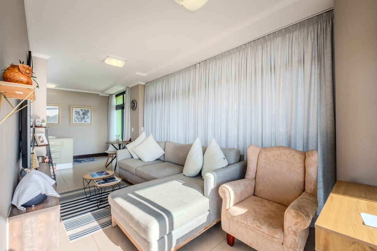 A bright and well-maintained living room featuring neutral tiled flooring, recessed ceiling lighting, and full-length window treatments.