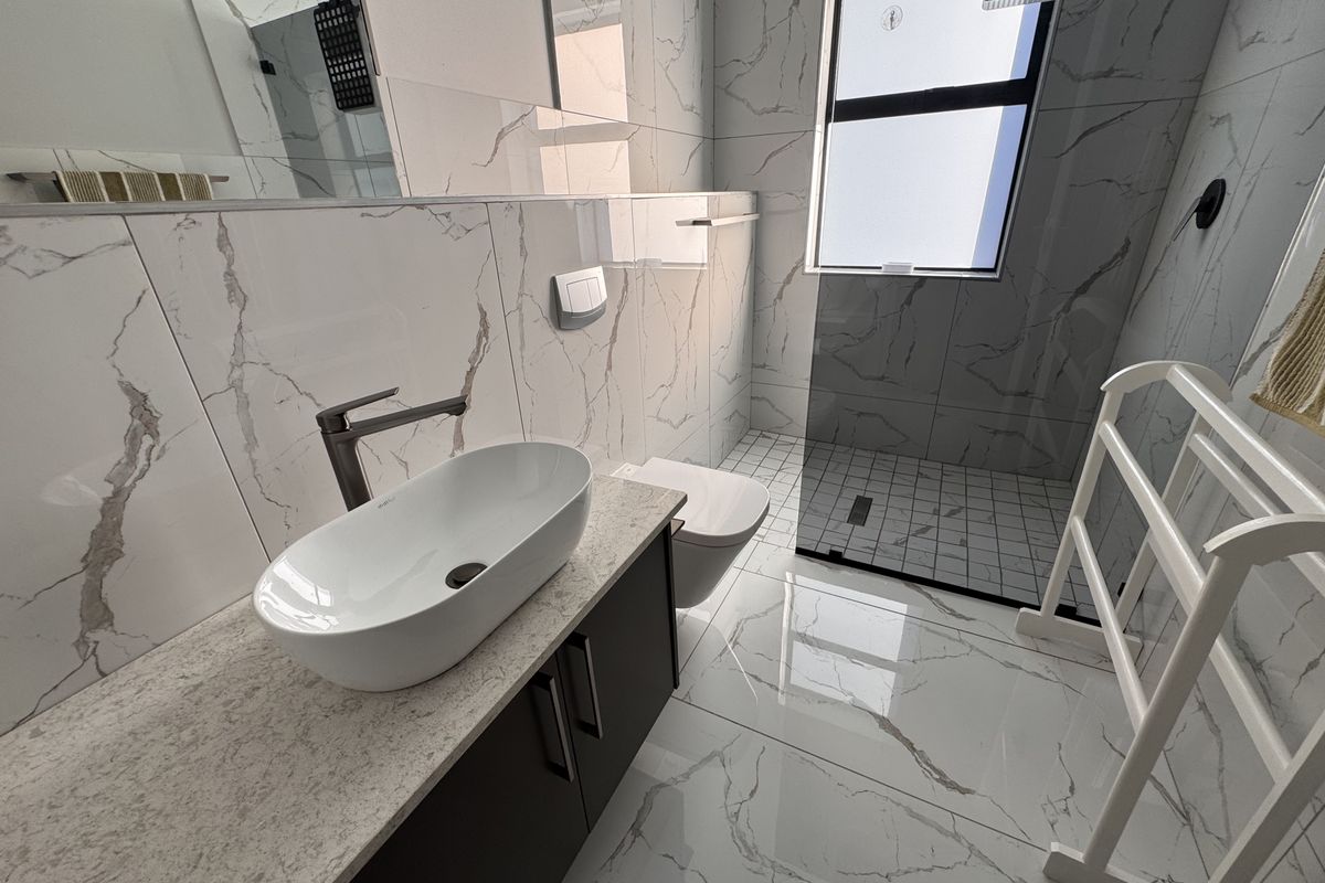 Modern bathroom featuring marble-look wall and floor tiles, a sleek vessel sink on a stone vanity, and a spacious walk-in shower with glass screen.