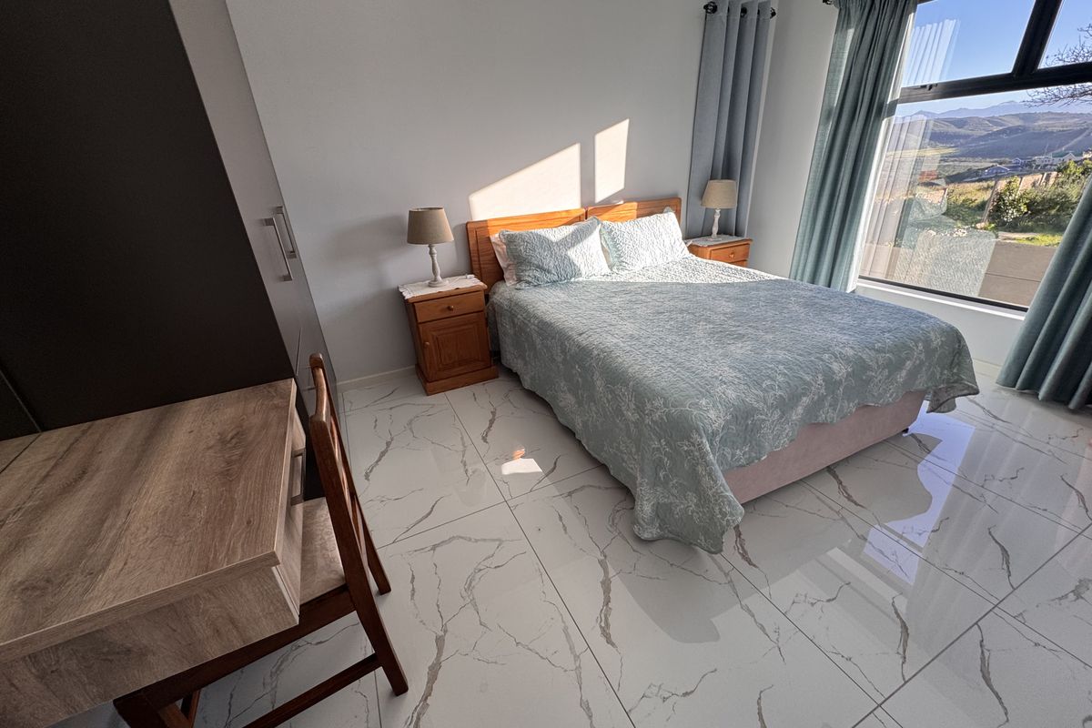A bright bedroom featuring modern large-format marble-look floor tiles, built-in cupboards, and a large window with scenic views.