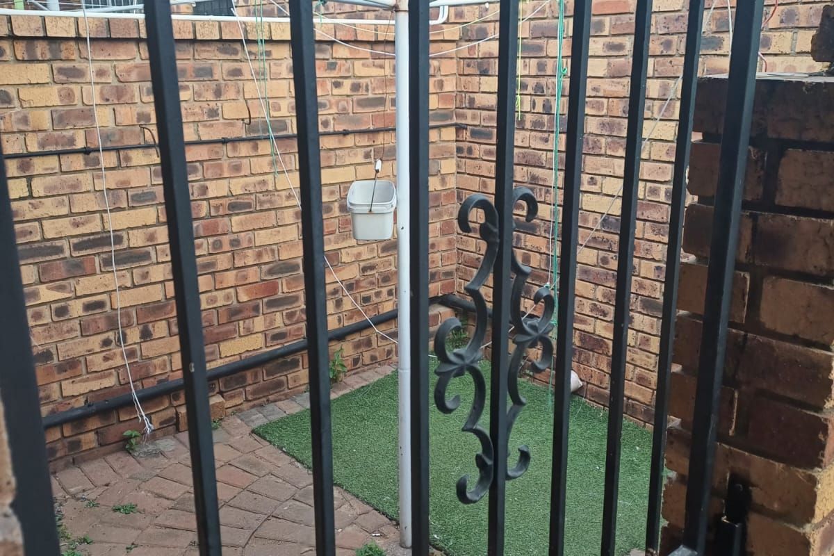 A private rear courtyard featuring brick boundary walls, paved flooring, and a metal security gate, providing a functional outdoor utility space.