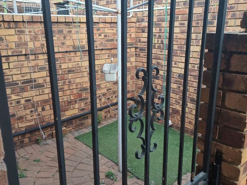 A private rear courtyard featuring brick boundary walls, paved flooring, and a metal security gate, providing a functional outdoor utility space.