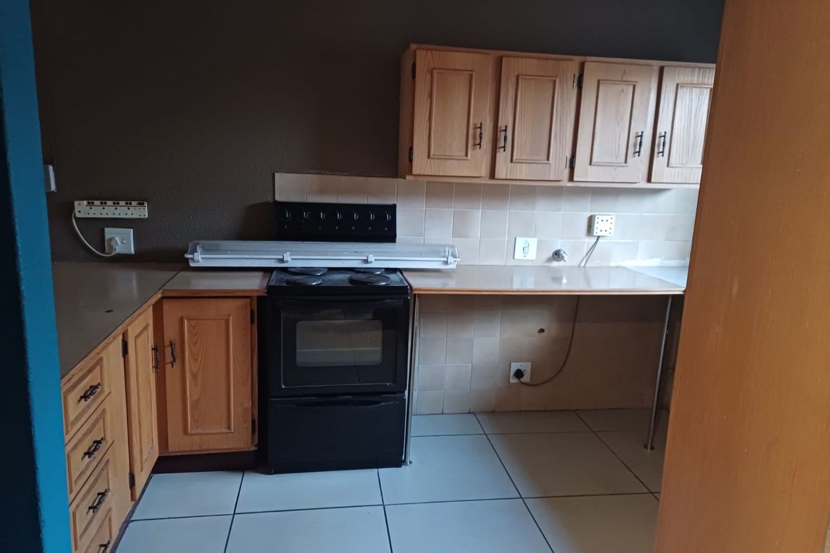 A dated kitchen featuring wooden cabinetry, tiled splashbacks, and a freestanding oven, offering a functional layout ready for modern renovation and cosmetic updates.
