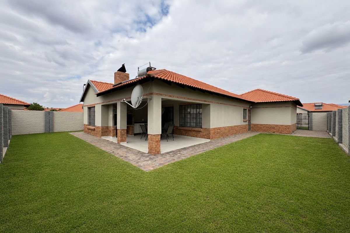Rear view of the house featuring a covered patio with a built-in braai, terracotta tiled roof, and a well-maintained lawn with boundary walls.