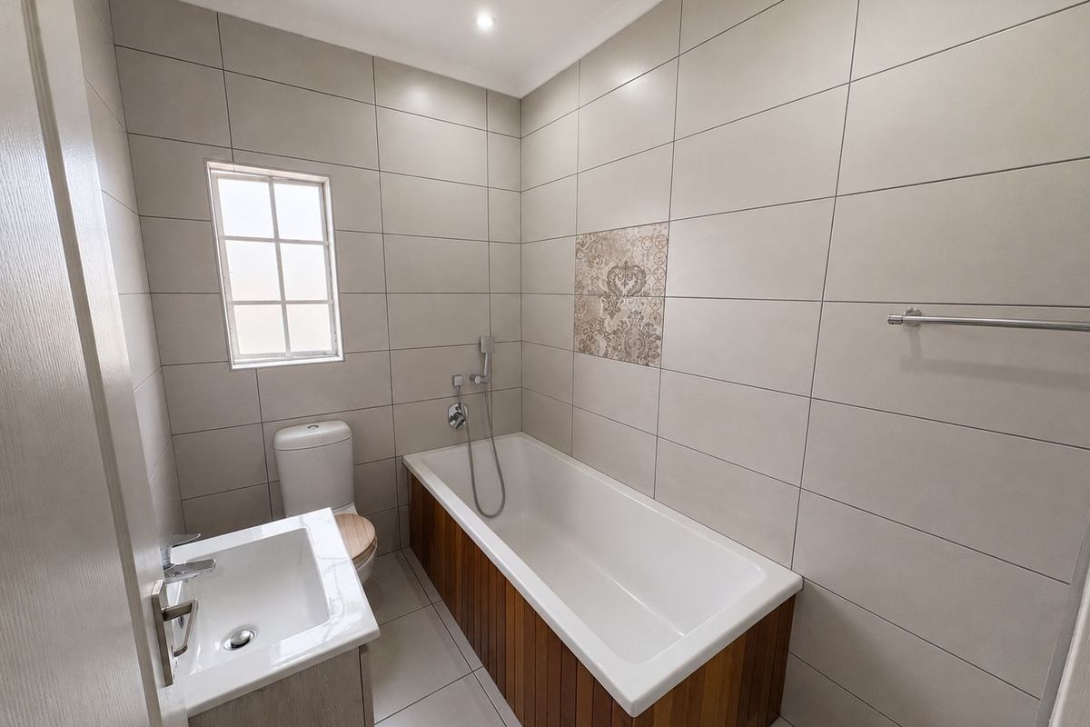 Modern bathroom featuring a built-in bathtub with wood-panel finish, vanity sink, toilet, and neutral wall tiling.