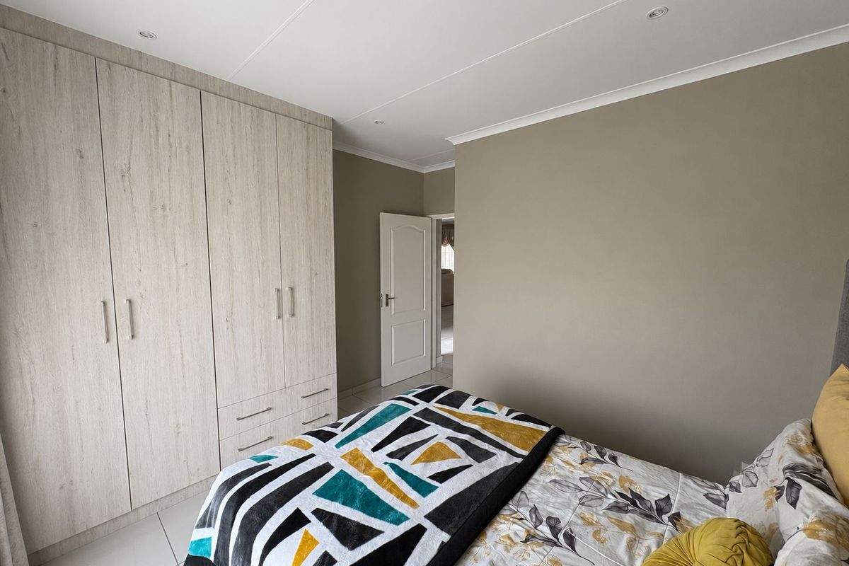 A well-maintained bedroom featuring neutral wall tones, modern built-in cupboards, tiled flooring, and recessed ceiling lighting.