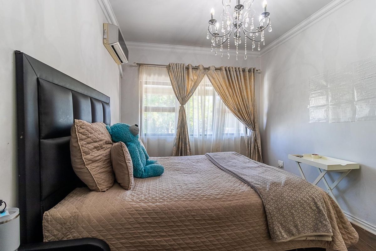 A bedroom featuring a wall-mounted air conditioning unit, crown molding, and a central chandelier fixture.