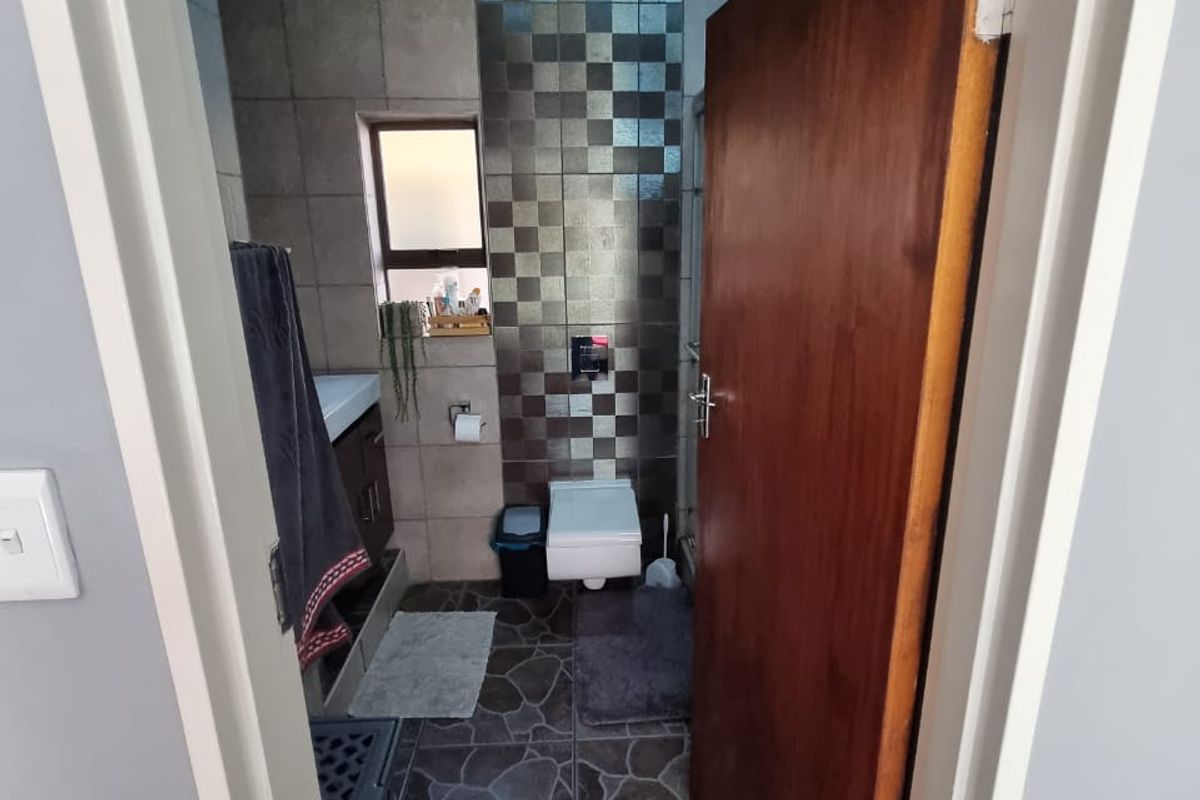 A compact bathroom featuring a wall-mounted toilet, vanity cabinet, and decorative tiled wall accents with stone-look floor tiles.