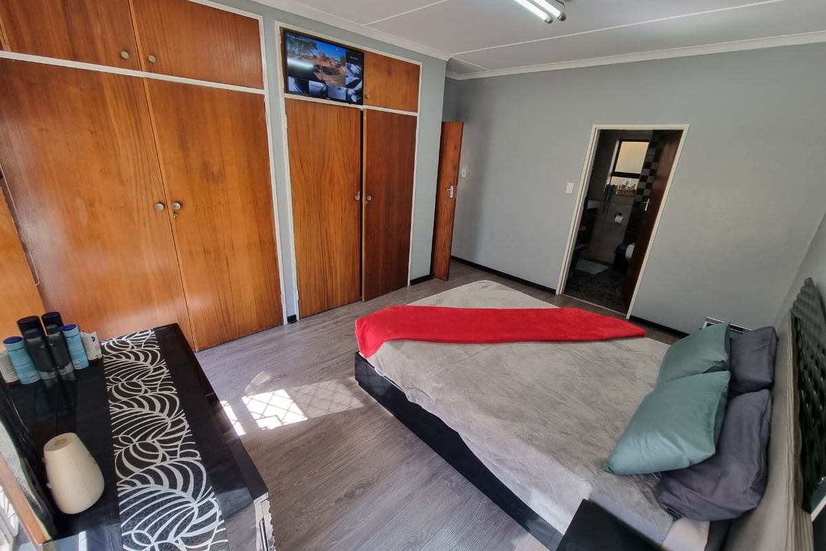 A bedroom featuring built-in wooden cupboards, laminate flooring, and direct access to an en-suite bathroom.