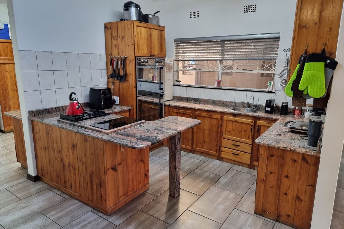 A functional kitchen featuring wooden cabinetry, granite countertops, a built-in oven, gas hob, and tiled flooring with a neutral backsplash.