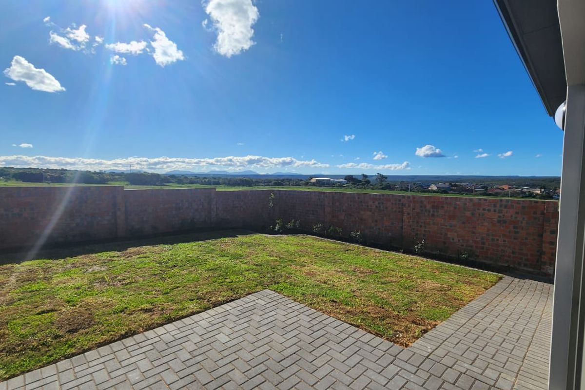 A rear garden featuring a paved patio area, a lawn, and a perimeter brick wall with expansive landscape views.