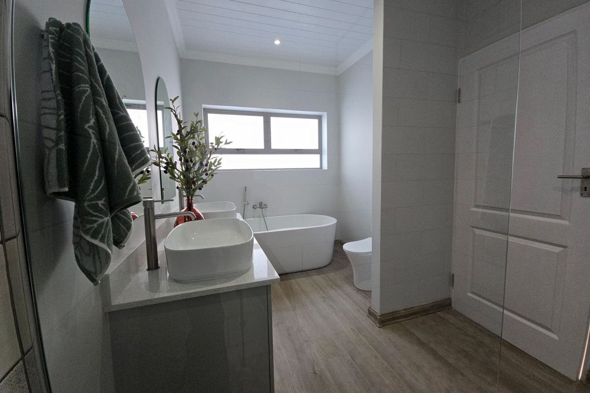 Modern bathroom featuring a freestanding bathtub, dual vessel sinks on a vanity, and wood-look flooring with clean, contemporary finishes.