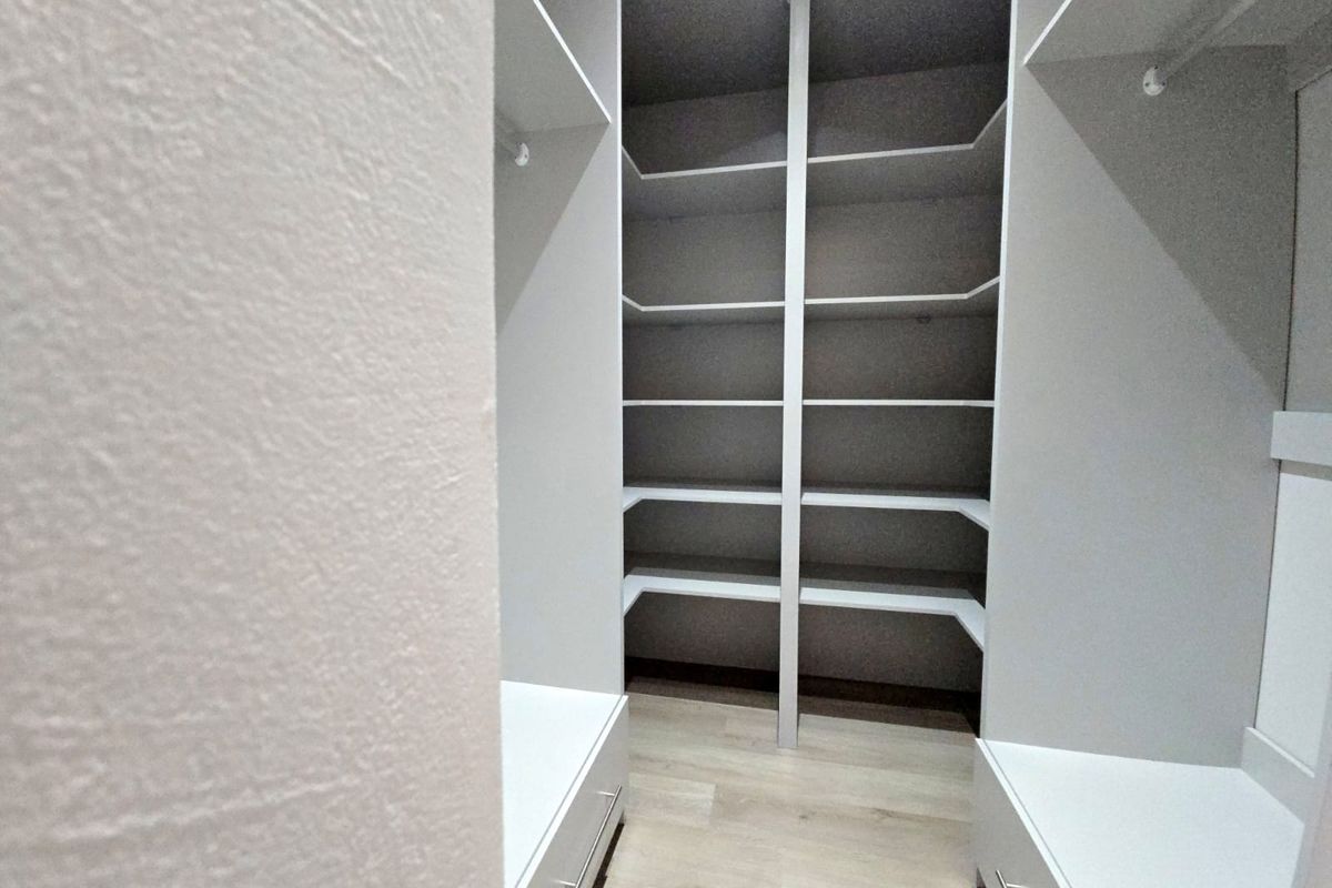 A modern, well-organized walk-in closet featuring custom built-in shelving, hanging rails, and integrated storage drawers with a clean, minimalist aesthetic.