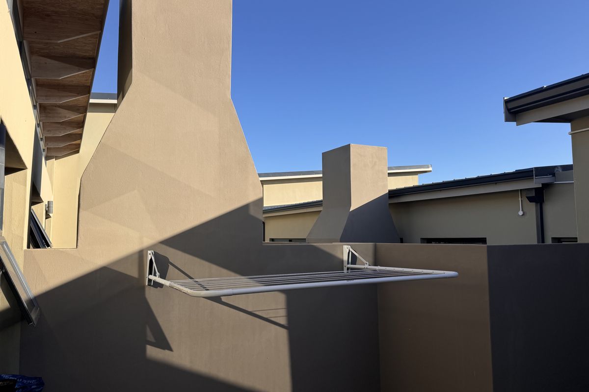 A view of the exterior building facade featuring a wall-mounted drying rack and prominent chimney structures against a clear blue sky.