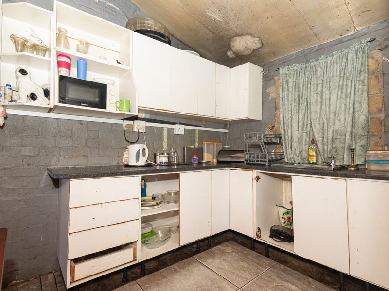 A dated kitchen featuring exposed brick walls, basic cabinetry, and tiled flooring, requiring significant renovation and cosmetic updates to improve functionality and aesthetic appeal.