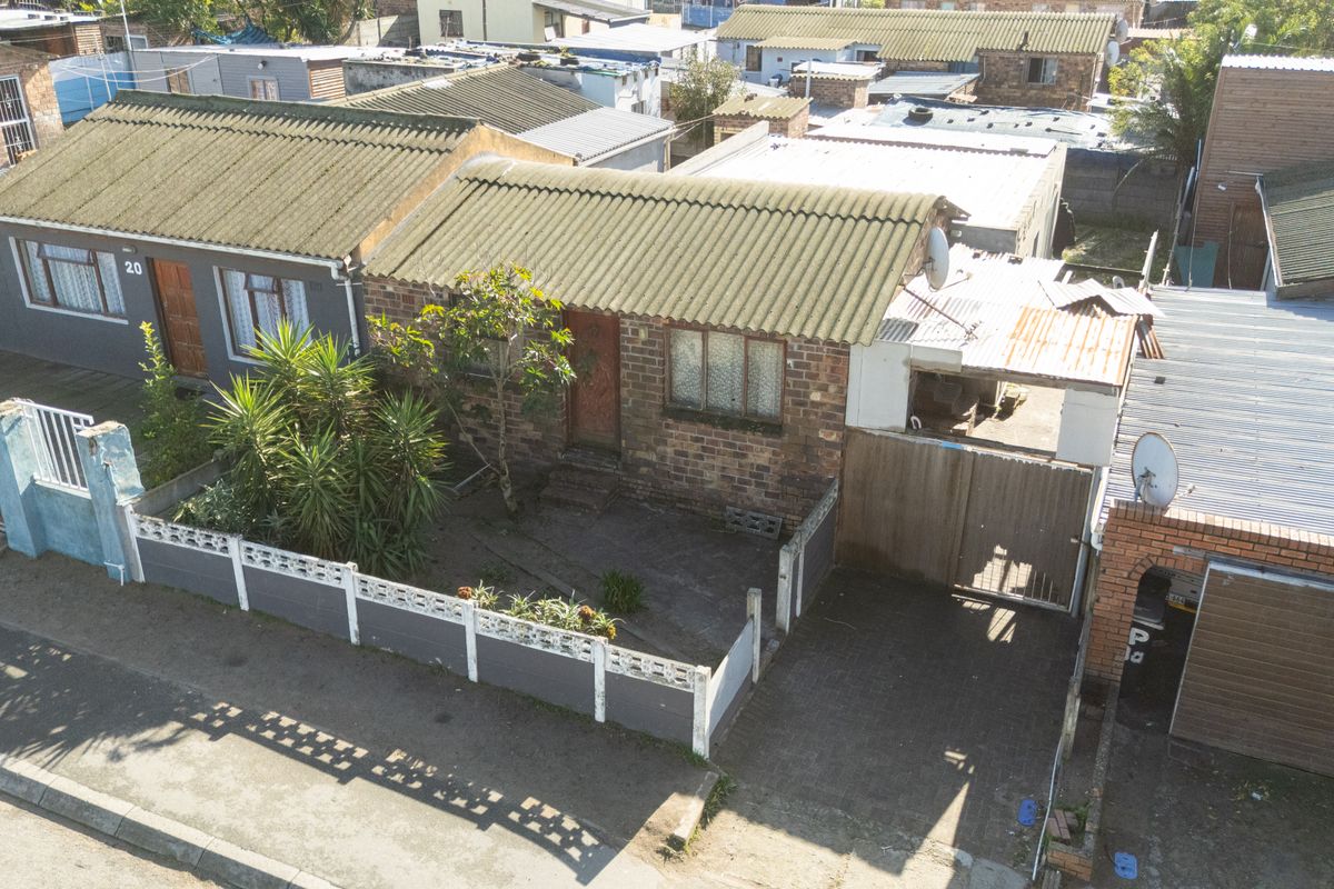Aerial view of a townhouse property featuring a brick facade, corrugated roof, paved driveway, and perimeter boundary walling.