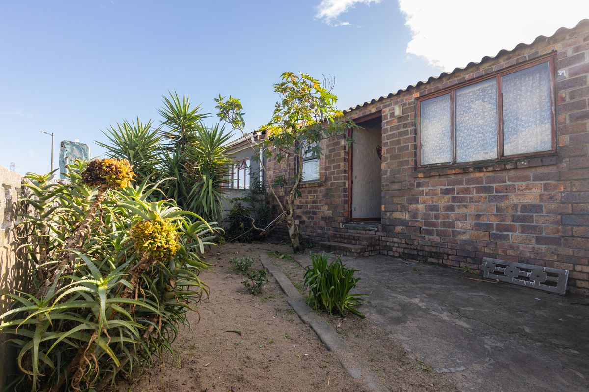 Rear exterior view of the townhouse featuring a face brick facade, concrete patio area, and established garden beds.