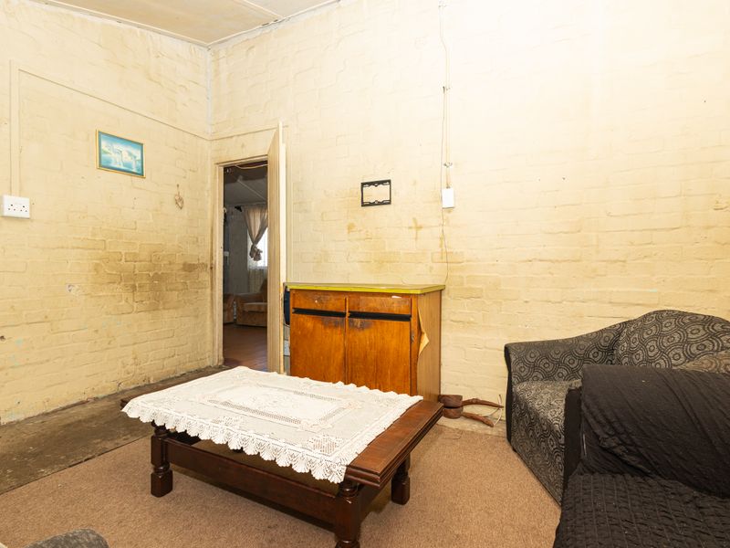 A living room featuring exposed brick walls and a doorway leading to an adjacent space, requiring cosmetic updates and wall repairs.