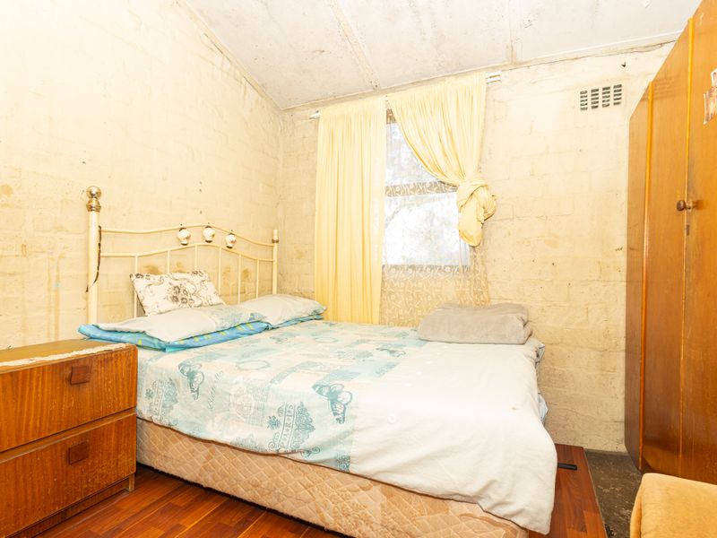 A bedroom featuring exposed brick walls, timber flooring, and a window with natural light. The space requires cosmetic updates to improve its overall condition.